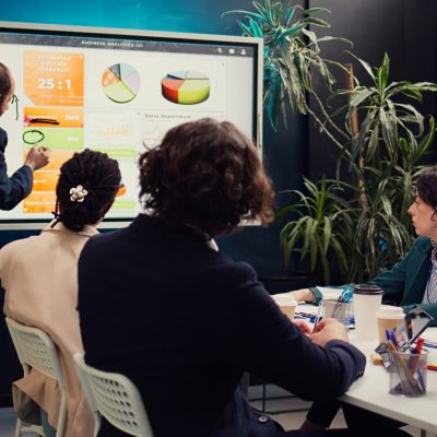 Sales manager creates a presentation to pitch in a new strategy for development, using interactive board to make his staff members understand the objectives. Business planning meeting. Camera B.